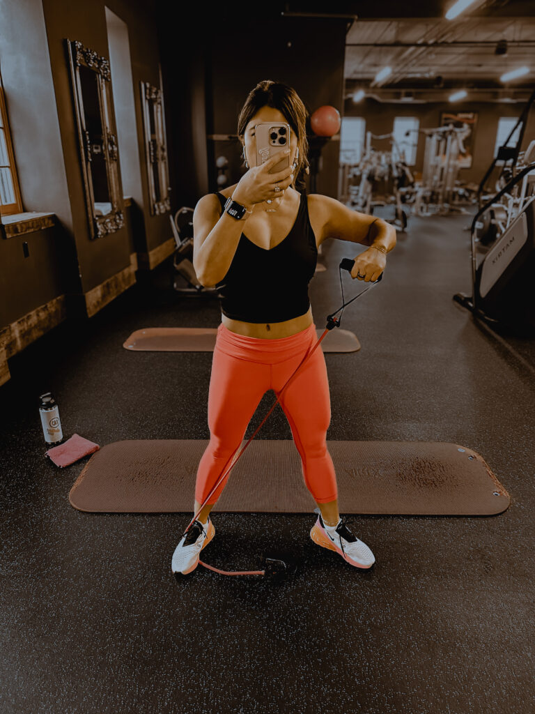 Tiffany Cooley taking a mirror photo at the gym wearing her ?URA Ring, after a strength workout. The image represents daily wellness habits, consistency, and how wearable tech supports active lifestyles.